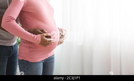 Gros plan sur la hug africaine de couple enceinte, debout à côté de la fenêtre Banque D'Images