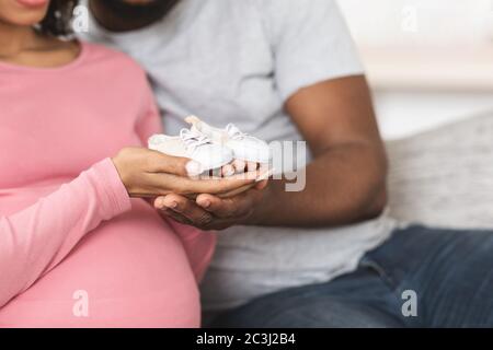 Gros plan de chaussures pour bébés dans les mains noires d'homme et de femme Banque D'Images