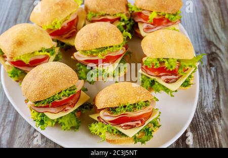 Délicieux sandwichs préparés avec un rouleau de ciabatta au jambon, au fromage, à la laitue et à la tomate sur une assiette blanche. Banque D'Images