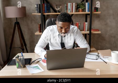 Un jeune homme d'affaires africain prospère assis à son bureau, travaillant sur un ordinateur portable Banque D'Images