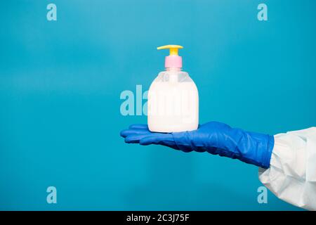 Personne main dans le gant bleu tenir le flacon de savon isolé sur fond bleu. Hygiène des mains virus propagation prévention pandémique Banque D'Images