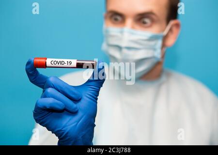 Le médecin, dans un masque de protection et des gants isolés sur fond bleu, tient le tube à essai contenant un échantillon de sang qui a été testé pour le coronavirus. Laboratoire t Banque D'Images