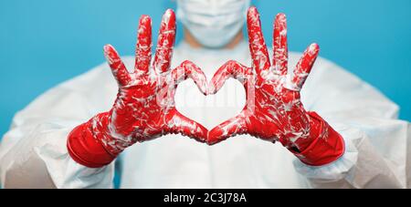 Médecin en costume médical masque de protection et gants, montrer le symbole du coeur avec la main dans la mousse de savon isolée sur fond bleu. Hygiène des mains, tartiner virus Banque D'Images