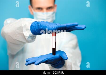 Le médecin, dans un masque de protection et des gants isolés sur fond bleu, tient le tube à essai contenant un échantillon de sang qui a été testé pour le coronavirus. Laboratoire t Banque D'Images