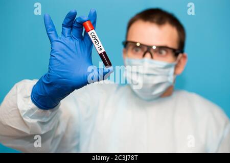 Le médecin, dans un masque de protection et des gants isolés sur fond bleu, tient le tube à essai contenant un échantillon de sang qui a été testé pour le coronavirus. Laboratoire t Banque D'Images