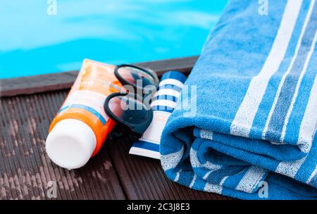 lunettes de soleil, tube de crème solaire, serviette bleue près de la piscine, fond tropical Banque D'Images
