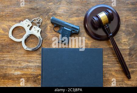 Droit, crime, peine. Juge, arme de poing, menottes et livre juridique vierge sur fond de bureau en bois, vue du dessus, espace pour les copies. Banque D'Images