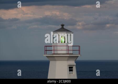 La salle de montre d'un phare vintage à huit côtés. La salle de lanterne a une grande ampoule verte. Le bâtiment en béton est blanc avec un rail rouge autour du dessus Banque D'Images