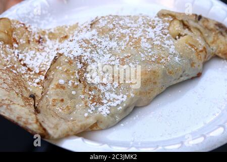 Crêpe à dessert avec sucre en poudre, garée de banane, chocolat et fraises sur une assiette en plastique Banque D'Images