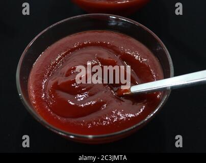 Ketchup dans un bol en verre avec louche sur fond noir Banque D'Images