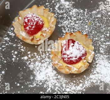 Tarte aux framboises avec crème et sucre en poudre dans une tasse à pâtisserie Banque D'Images