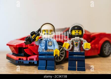 POZNAN, POLOGNE - 01 mai 2020 : figurine LEGO Toy police parlant sur talkie walkie à côté d'un homme à tête avec menottes devant une Ferrari rouge Banque D'Images