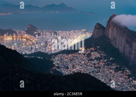 Vue de nuit ou Favela Rocinha dans la montagne et le district d'Ipanema derrière à Rio de Janeiro, Brésil. Banque D'Images