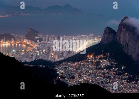 Vue de nuit ou Favela Rocinha dans la montagne et le district d'Ipanema derrière à Rio de Janeiro, Brésil. Banque D'Images