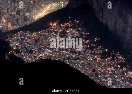 Vue de nuit ou Favela Rocinha dans la montagne et le district d'Ipanema derrière à Rio de Janeiro, Brésil. Banque D'Images