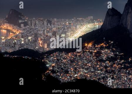 Vue de nuit ou Favela Rocinha dans la montagne et le district d'Ipanema derrière à Rio de Janeiro, Brésil. Banque D'Images