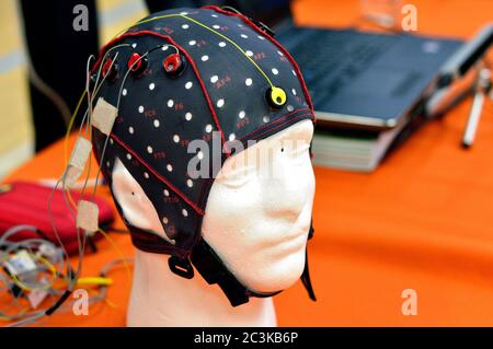 Tête d'électroencéphalogramme (EEG) avec disques métalliques plats (électrodes) fixés à un modèle de tête avec ordinateur portable flou à l'arrière-plan. Banque D'Images