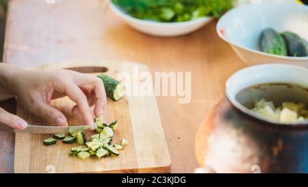 Femme coupant le concombre vert sur une planche de bois à l'extérieur. Gros plan des mains des femmes coupant des légumes avec un couteau sur la planche à découper. Banque D'Images