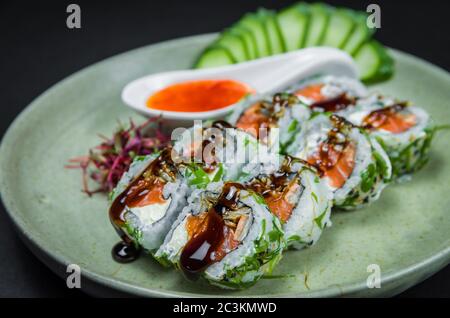 Sushis parfaits, cuisine japonaise traditionnelle. Délicieux uramaki avec sauce aigre-douce sur l'assiette décorée, fond noir. Banque D'Images
