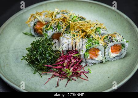Sushi, cuisine japonaise traditionnelle. Délicieux uramaki sur plaque décorée, fond noir. Banque D'Images