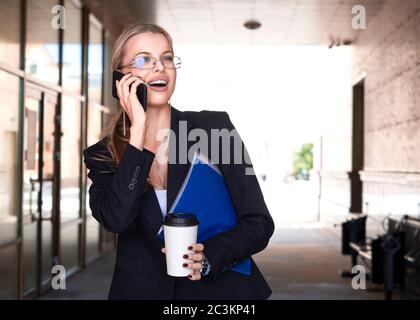 Gros plan portrait d'une femme dans un costume d'affaires parlant téléphone mobile tout en marchant dans la rue dans le quartier des affaires de la ville. Banque D'Images