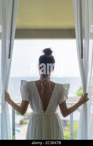 Gril thaïlandais le whirt robe ling code vestimentaire est debout en face de la chambre à coucher avec terrasse et piscine simming phanoramic sur la mer en face d'elle. Banque D'Images