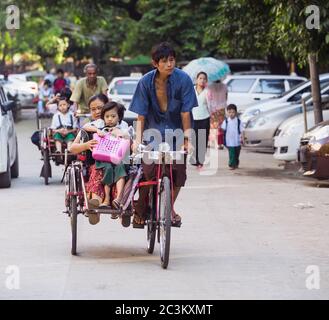 YANGON, MYANMAR - 13 NOVEMBRE 2014 : enfants emmenés à l'école à bord de cyclos. Le cyclo est un mode de transport important dans la capitale du Myanmar Banque D'Images