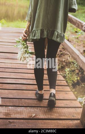 Photo verticale d'une femelle tenant une belle fleur blanche marche le long d'un quai en bois Banque D'Images