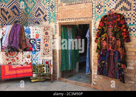 Cour intérieure du Registan avec des manteaux traditionnels ouzbek colorés accrochés près de la porte et variété de suzani, Samarkand, Ouzbékistan Banque D'Images