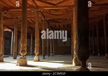 Belles colonnes en bois avec des sculptures élégantes et le rayon de lumière brillant dans l'ancienne mosquée Juma, Khiva, Ouzbékistan Banque D'Images