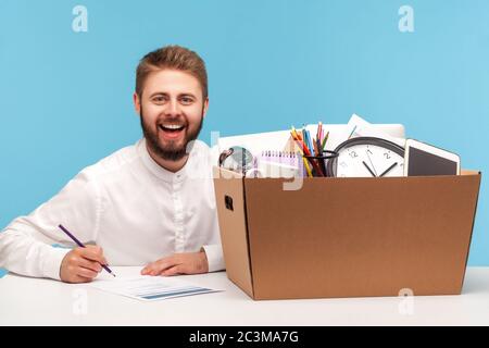 Heureux homme chanceux assis sur le lieu de travail avec boîte d'effets personnels et souriant à la caméra, se sentant excité motivé par l'occasion de nouveau travail, de promotion et Banque D'Images