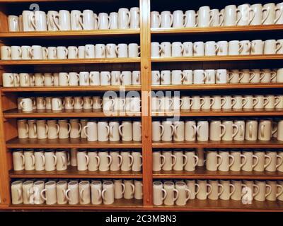De nombreuses grandes tasses à bière blanche sont posées sur une étagère dans un pub. Banque D'Images