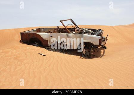 L'épave de véhicules en 4x4 (quatre roues motrices) rouillés et partiellement enfoui dans les dunes de sable du désert arabe. Le sable est lentement en train d'engloutir l'épave. Banque D'Images