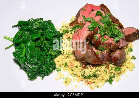 plat nord-africain d'agneau avec couscous et épinards sur fond blanc Banque D'Images