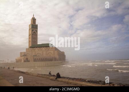 Un groupe de personnes marchant et assis autour de la mosquée Hassan II à Casablanca, au Maroc, pendant un après-midi brumeux, profitant de la vue sur l'océan Banque D'Images