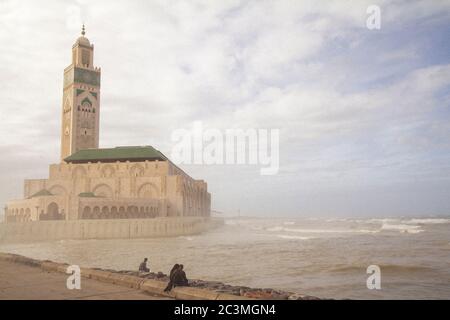 Un groupe de personnes marchant et assis autour de la mosquée Hassan II à Casablanca, au Maroc, pendant un après-midi brumeux, profitant de la vue sur l'océan Banque D'Images