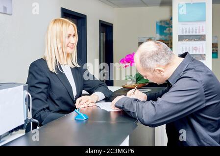 femme secrétaire gérant au bureau de la réception. homme remplit les documents Banque D'Images