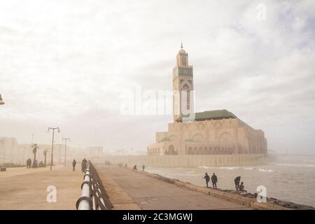 Un groupe de personnes marchant et assis autour de la mosquée Hassan II à Casablanca, au Maroc, pendant un après-midi brumeux, profitant de la vue sur l'océan Banque D'Images