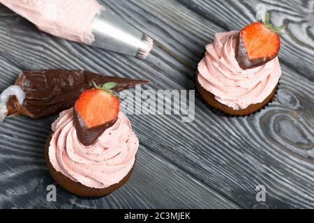 Petits gâteaux au chocolat et crème à la fraise. Décoration avec demi-fraises au chocolat. Banque D'Images