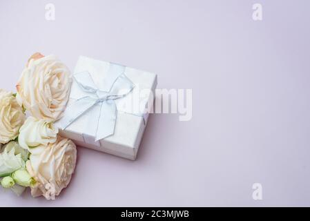 Un petit cadeau à côté de délicates fleurs roses sur fond rose. Carte cadeau pour la Saint-Valentin. Banque D'Images