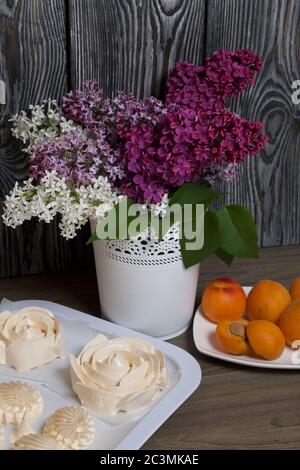 Guimauves et abricots. Près d'un bouquet de lilas de différentes couleurs. Sur le fond des planches de pin peintes. Banque D'Images