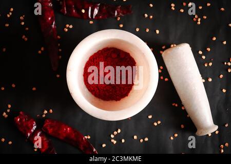Couche plate de piment rouge séché et écrasé ou de poudre de Cayenne au piment rouge dans du mortier de pierre avec des pilon et des graines de piment isolées sur fond noir. Banque D'Images