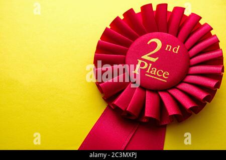 Rosette de ruban rouge pour la deuxième place dans un concours ou une course sur un fond jaune avec espace de copie Banque D'Images
