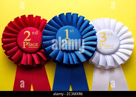 Trois rosettes pour le gagnant et les deuxième et troisième coureurs placés dans une compétition ou course mise côte à côte sur un fond jaune Banque D'Images