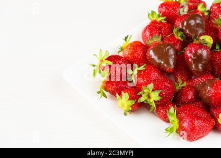 Fraises enrobées de délicieux chocolat dans un plat blanc isolé sur fond blanc. Vue rapprochée. Banque D'Images