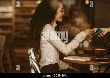 Femme au café payant sa facture à l'aide d'un téléphone portable et d'un lecteur électronique. Client féminin payant à l'aide de la technologie NFC dans un café. Banque D'Images