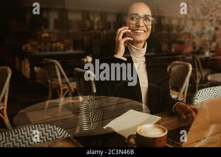 Femme assise au café et parlant sur un téléphone portable. Femme d'affaires parlant avec le client pendant qu'elle travaille dans un café. Banque D'Images