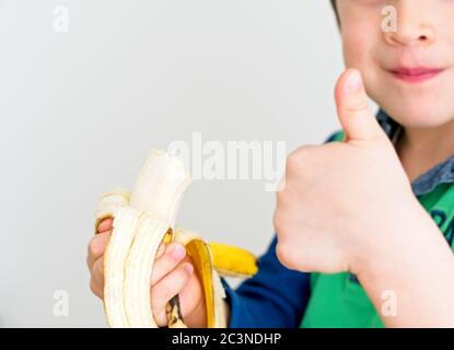 Un garçon caucasien mangeant une banane et avec son pouce vers le haut montrant qu'il est correct avec un fond blanc Banque D'Images