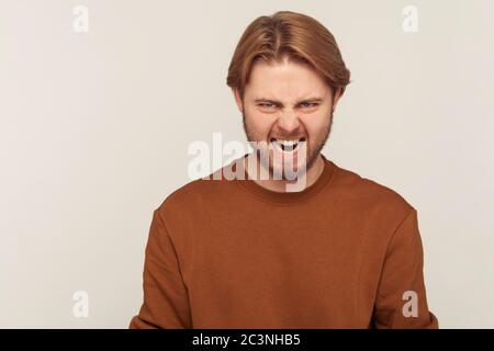 Portrait d'un homme barbu agacé dans un sweat-shirt qui tourne à l'intérieur de l'appareil photo, exprimant une forte irritation de colère, hurlant fou et plein de haine Banque D'Images