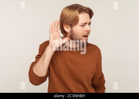 Quoi ? Je ne vous entends pas ! Portrait d'un homme barbu dans un sweat-shirt, main près de l'oreille et à l'écoute du chuchotement, difficile à comprendre parler tranquillement Banque D'Images